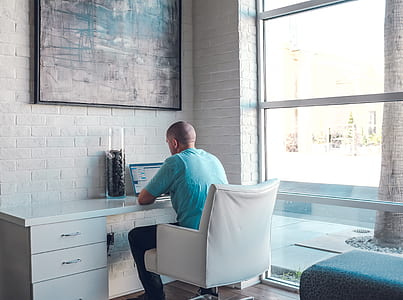 man sitting on chair using laptop beside glass panel thumbnail