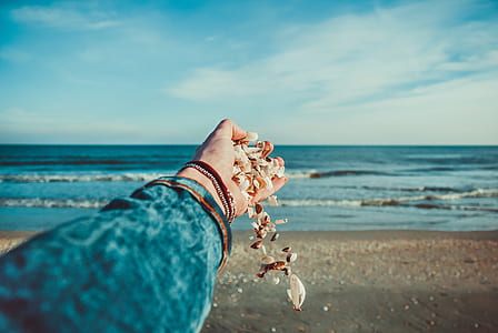 selective focus photography of person releasing pebbles on seashore thumbnail