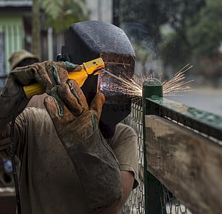 person wearing welding mask welding on green metal frame thumbnail