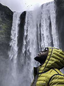 Photography of Man Wearing Bubble Hoodie Jacket Near Waterfalls thumbnail