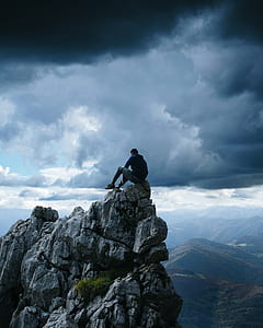 man sitting on cliff under nimbus clouds thumbnail