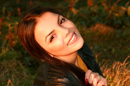 smiling woman wearing black leather jacket holding hair thumbnail
