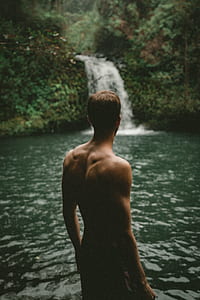 topless man standing next to waterfalls in forest thumbnail