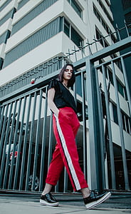 woman walking near gray fence and building during daytime thumbnail