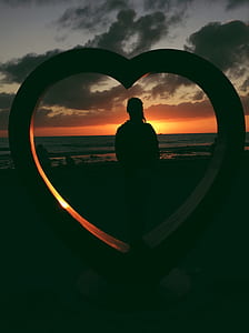 silhouette photo of woman facing body of water beside heart standee thumbnail