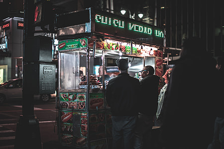 people buying hotdogs from hotdog stand on a street at night thumbnail