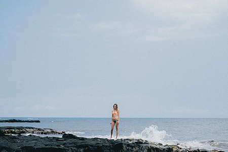 woman wearing bikini standing on coastal rock during daytime thumbnail