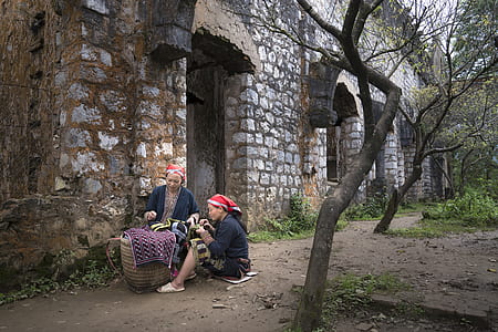 two woman near brown barrel beside concrete building during daytime thumbnail