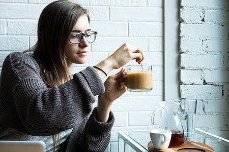 woman stirring coffee on clear glass mug beside table thumbnail