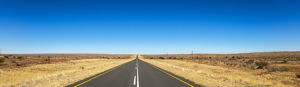 straight road between land mass under blue sky at daytime thumbnail