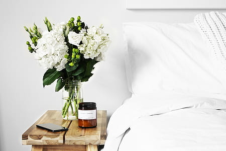 white petaled flowers on vase on top of nightstand beside smartphone and bottle near to bed thumbnail