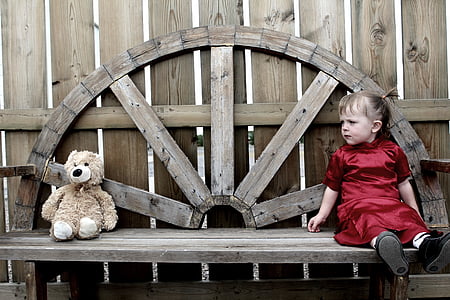 girl sitting on brown wooden bench while looking at brown bear plush toy thumbnail