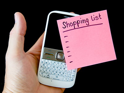 person holds white QWERTY phone and pink sticky note thumbnail