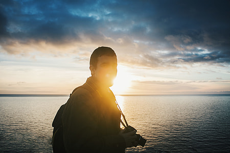 man holding black DSLR camera near body of water thumbnail