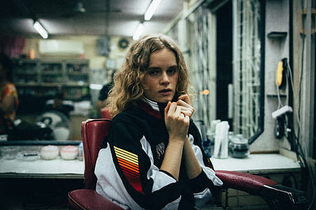 woman in black, white, and red jacket sits on red armchair in a salon near a mirror thumbnail