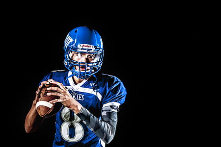 Man Holding Football and Football Uniform in Black Background thumbnail