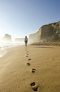 woman in white sleeveless top walking on gray sand beach thumbnail