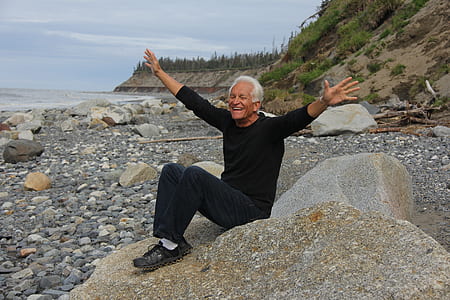 man sitting on gray stone near seashore thumbnail