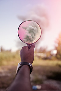 person holding magnifying glass pointed towards smoke during daytime thumbnail