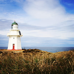 white lighthouse on cliff under blue sky thumbnail