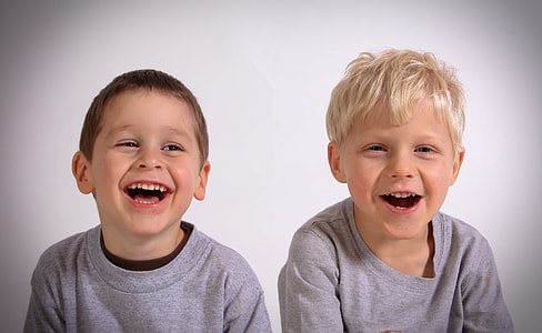 two toddlers wearing heather gray tops smiling near white wall thumbnail