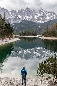 man in blue jacket standing beside body of water thumbnail