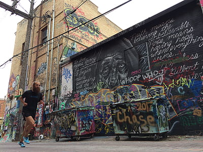man running near two dumpsters and wall with graffiti thumbnail