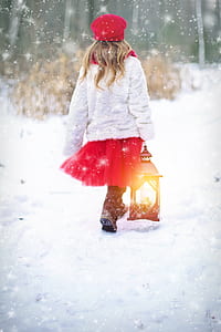 girl wearing white sweater and red tutu skirt walking on snow covered ground holding lantern thumbnail
