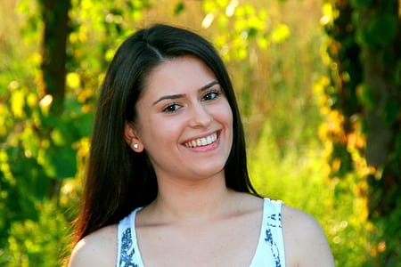 woman in white scoop-neck sleeveless top smiling while surrounded with green plants thumbnail