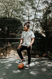 man in gray shirt and black pants stepping on basketball during daytime thumbnail