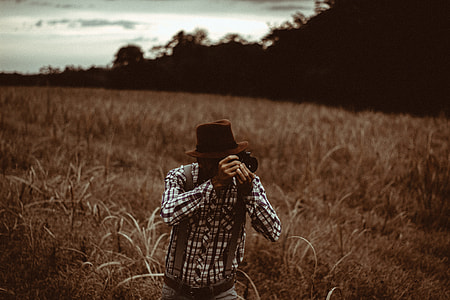 man using camera while standing on grass field thumbnail