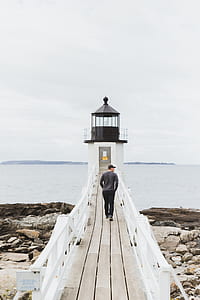 man walking on brown dock going to lighthouse thumbnail