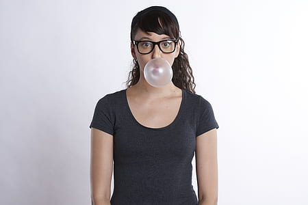 woman in black scoop-neck shirt blowing chewing plastic balloon with white background on focus photo thumbnail