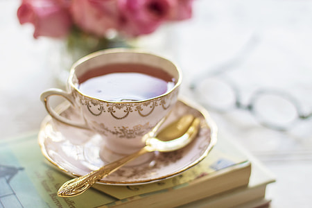 white and brown ceramic teacup with tea beside spoon on top of book thumbnail