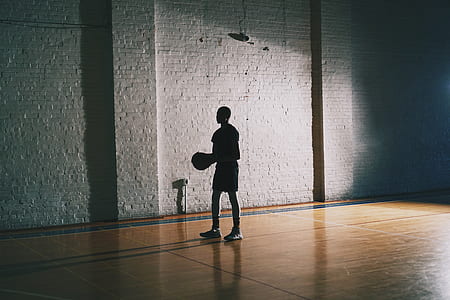 silhouette photo of man on basketball court holding ball thumbnail