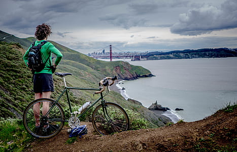 man standing on cliff beside road bicycle thumbnail