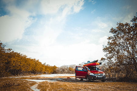 red hatchback parked near brown tree under white clouds and blue sky thumbnail