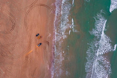 two black and one yellow cars parked at the seashore thumbnail