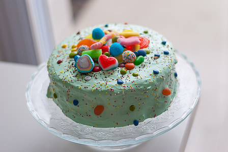 green icing-covered cake with multicolored toppings on glas cake dome thumbnail