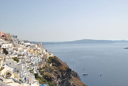white painted buildings on top of rocky mountain beside calm ocean under clear blue sky thumbnail