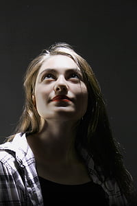 woman in white and black plaid collared top looking up inside dark room thumbnail