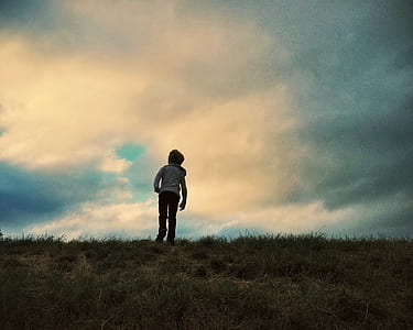 person in gray hoodie and black pants standing on green grass under blue cloudy skies thumbnail
