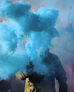 person in brown jacket holding yellow device with a blast of blue smoke thumbnail