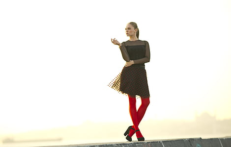 woman wears black long-sleeved dress with red leg stocking thumbnail