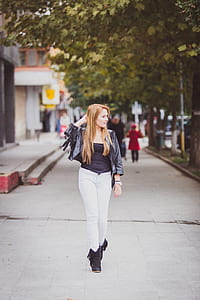 woman wearing black scoop-neck blouse, white fitted jeans and black boots outfit standing near trees at daytime thumbnail
