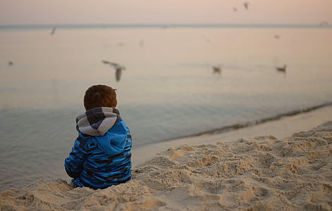 toddler sitting on sand beside body of water during daytime thumbnail