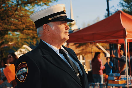 Man in Black Lapel Suit Jacket Wearing Police Cap Near Orange Canopy Tent thumbnail