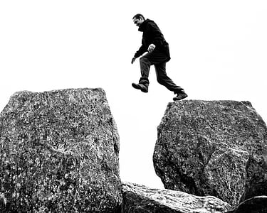 grayscale photo of man on top of rock formation thumbnail
