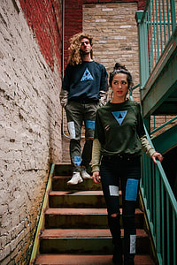 two man and woman wearing sweaters standing on stairs beside red painted wall thumbnail