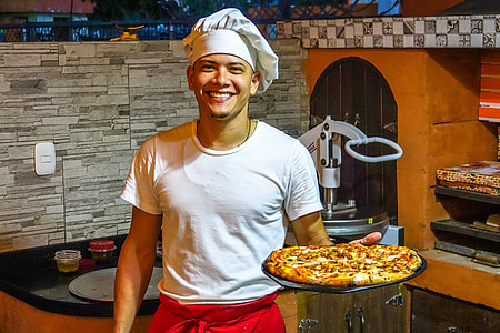 man holding baked pizza standing near black and brown wooden cabinet thumbnail